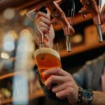 tattooed caucasian barman pouring beer while standing in pub.